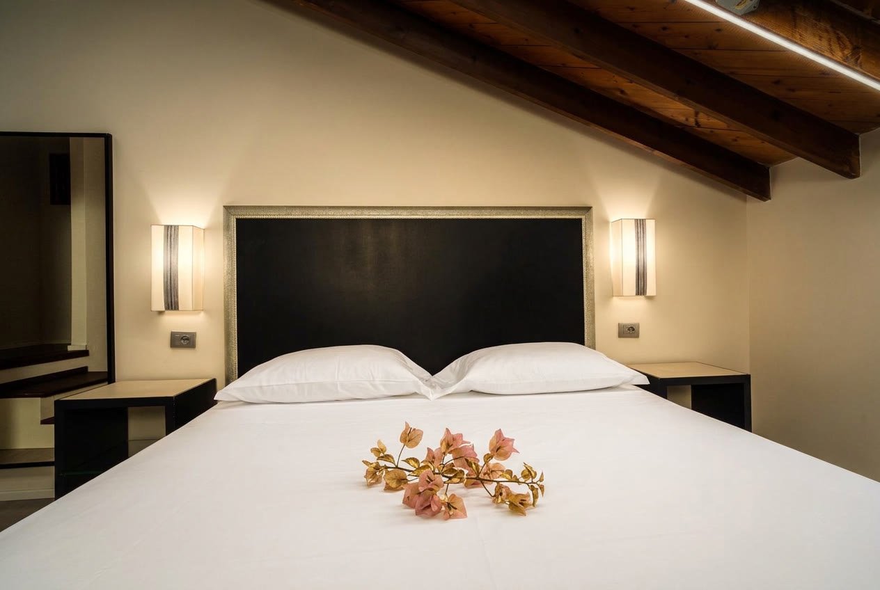 Ai Cannoni — letto matrimoniale con testiera scura e applique ai lati