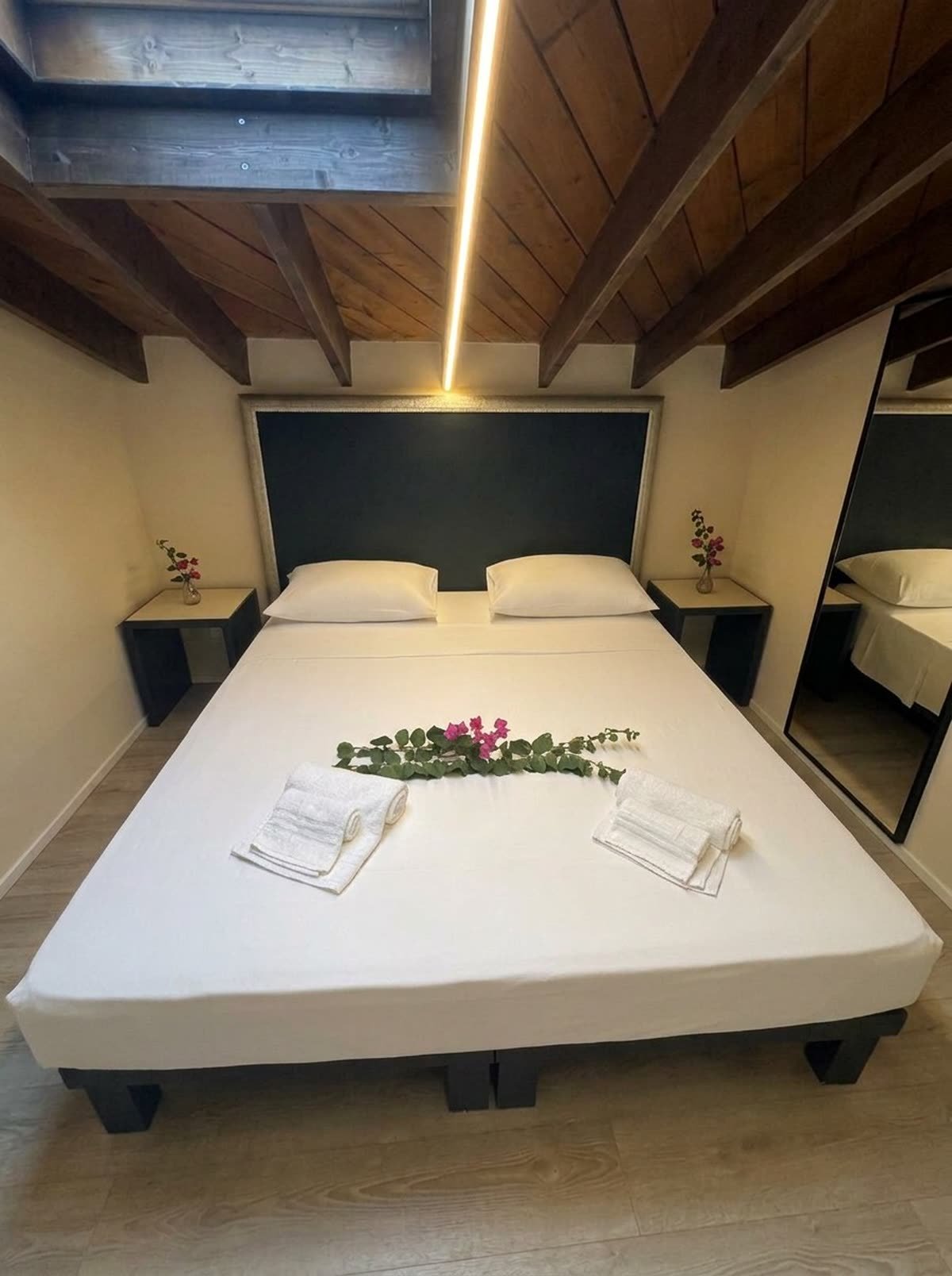 Al Castello — il letto con la testiera scura, gli asciugamani e i fiori freschi